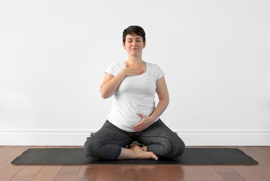 Pregnant woman in Easy Pose with one hand on her heart, a first trimester prenatal yoga pose
